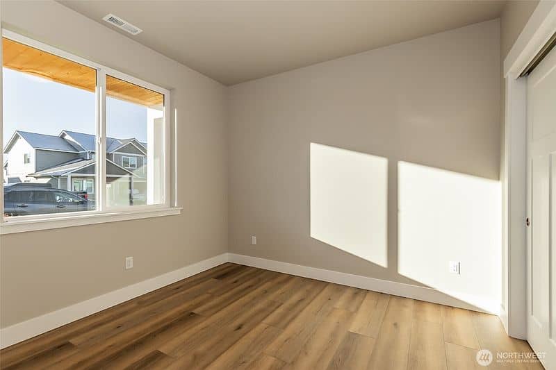 Bright empty room with large window and hardwood floor in new home.